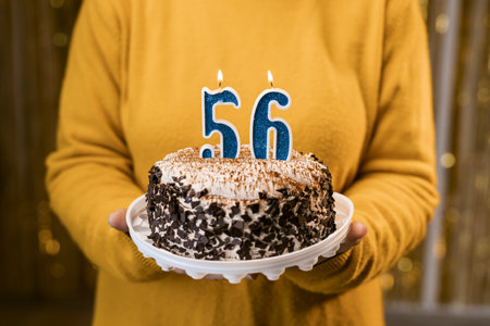 Woman holding a festive cake with number 56 candles while celebrating birthday party. Birthday holiday party people concept.の写真素材