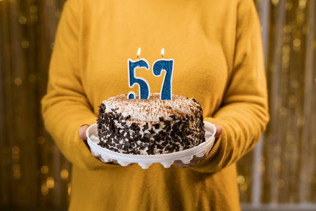 Woman holding a festive cake with number 57 candles while celebrating birthday party. Birthday holiday party people concept.の写真素材