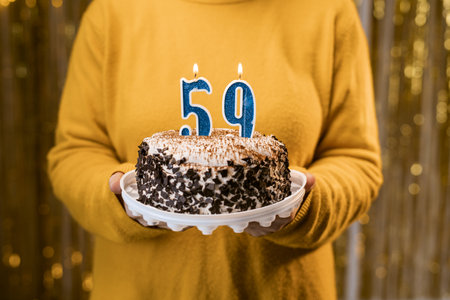 Woman holding a festive cake with number 59 candles while celebrating birthday party. Birthday party people concept. close-up viewの写真素材