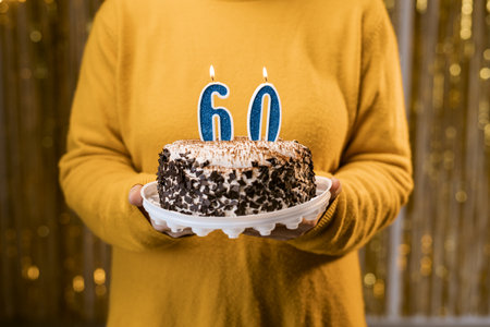 Woman holding a festive cake with number 60 candles while celebrating birthday party. Birthday party people concept. close-up viewの写真素材