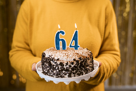 Woman holding a festive cake with number 64 candles while celebrating birthday party. Birthday party people concept. close-up viewの写真素材