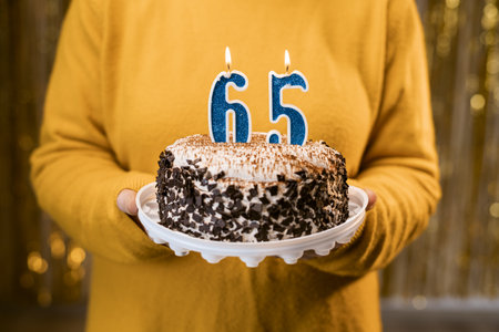Woman holding a festive cake with number 65 candles while celebrating birthday party. Birthday party people concept. close-up viewの写真素材