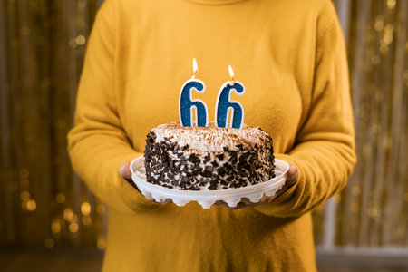 Woman holding a festive cake with number 66 candles while celebrating birthday party. Birthday party people concept. close-up viewの写真素材