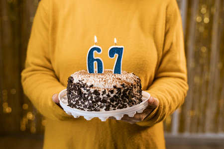 Woman holding a festive cake with number 67 candles while celebrating birthday party. Birthday party people concept. close-up viewの写真素材