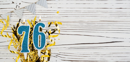Number 76 blue celebration candle on white wooden background with golden foil. Copy space.の写真素材