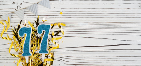 Number 77 blue celebration candle on white wooden background with golden foil. Copy space.の写真素材