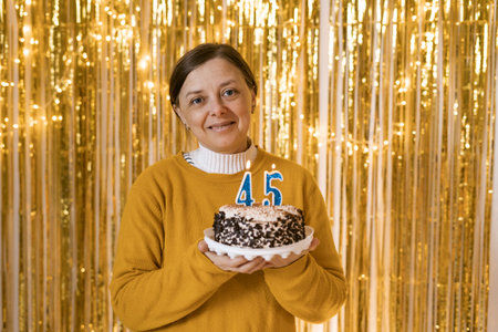 Smiling Middle aged woman with birthday cake with burnings candles number 45. Adult female celebration her birthday at home. Celebration party holidayの写真素材