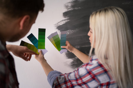 Young couple choosing color on palette for painting walls at new apartment, planning design of their new houseの写真素材