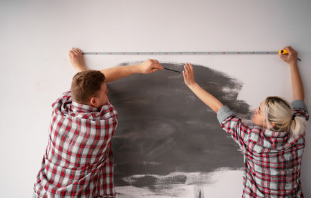 Young couple measuring wall in new home, rearview. Repair, construction and building conceptの写真素材
