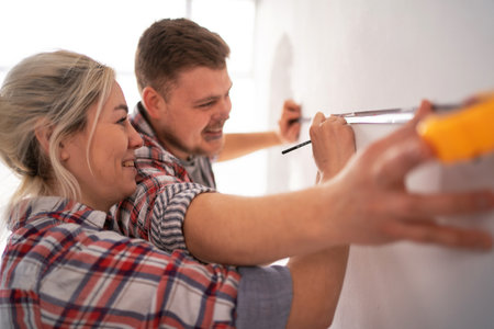 Close-up of young happy couple measuring wall with measurement tape and pencil repairing apartment. House renovationの写真素材