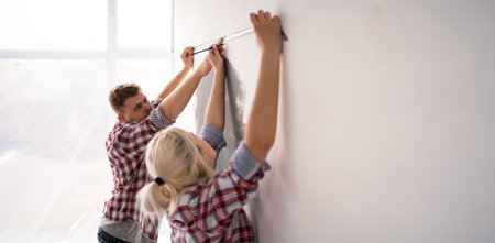 Young couple measure wall with measuring tape doing apartment repair together. Repair, building and home concept. Banner.の写真素材