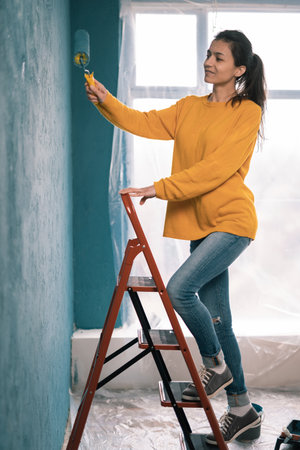 Young woman paints her walls blue using a roller. Painting a wall with paint roller. Interior wall of new house.の写真素材