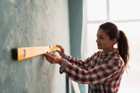 Caucasian woman checks wall level using spirit level. Home renovation concept.の写真素材
