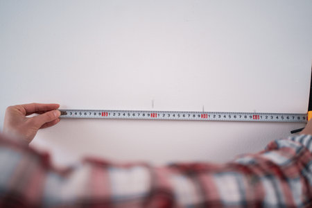 Female workman using tape measure for home renovation. Woman taking measure on the white wall. Measures wall with construction tape during home renovation.の写真素材