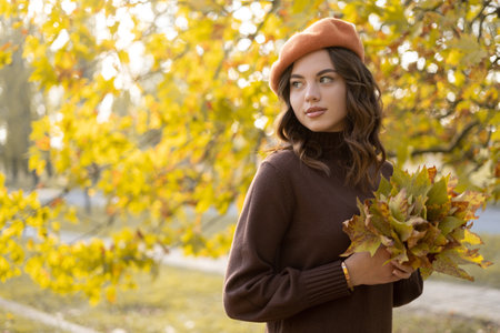 Portrait of beautiful young woman in autumn park with maple leaves in her hands. Walking outdoors in autumn.の写真素材