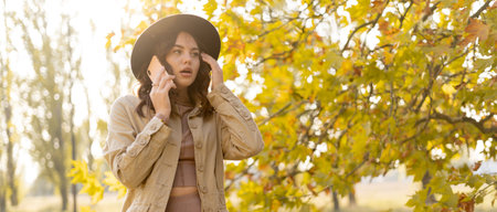 Frustrated young woman talking on phone standing in autumn park. Unhappy female talking over phone having problem. Copy space.の写真素材