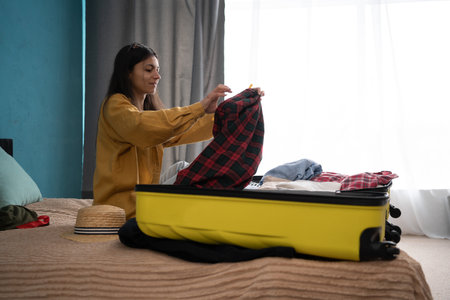 Summer holidays, vacation concept. Young happy woman packing summer clothes into suitcases on bed. Preparing travel items for new journey. copy spaceの写真素材