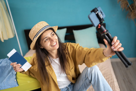 Female blogger recording vlog video with mobile phone live streaming preparing to travel sitting...