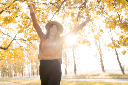 Young woman is having fun while walking through the forest on a sunny autumn day, plays with maple leaves while throws them up. copy spaceの写真素材