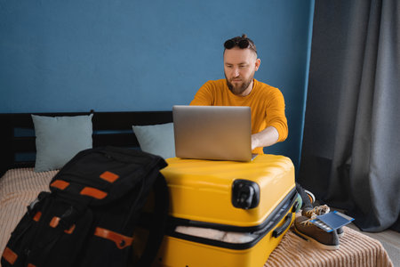 Travel man planning vacation trip, using computer booking hotel room online. Happy male tourist at home browsing rental holiday accommodation website on laptopの写真素材