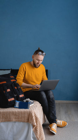 Male traveler getting ready for a summer holiday trip vacation searching for travel information using laptop in bedroom. Travel on holiday, summer vacation.の写真素材