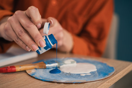 Close-up of female hands on a palette pouring blue acrylic paint. Vacation and hobby concept.の写真素材