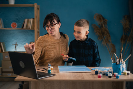 Online education for children. Mother and son schoolboy watching a video lecture on drawing using computer in the living room.の写真素材