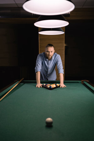 American billiard poule. Handsome man making triangle of billiard balls, getting ready to start a game. Playing billiard conceptの写真素材