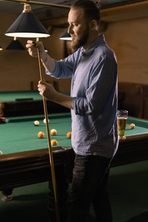 Attractive man snooker, billiard player, chalking the cue in motion with chalk. Professional hand...