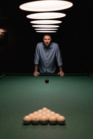 A bearded caucasian man stands near a billiard table preparing for the start of the game. Billiard...