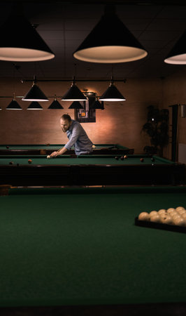 stylish caucasian bearded man playing billiards. stands near the table.