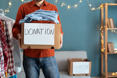 Caring male volunteer holding donation box full of clothes to needy people. Man preparing things in package donate to poor, those in need. Reuse, recycle, charity concept.の写真素材