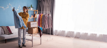 Young hispanic woman sorting clothing indoors at home. Charity donation concept.の写真素材