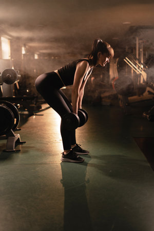 Fitness athletic woman doing exercises with dumbbells in the gym in the evening smokeの写真素材