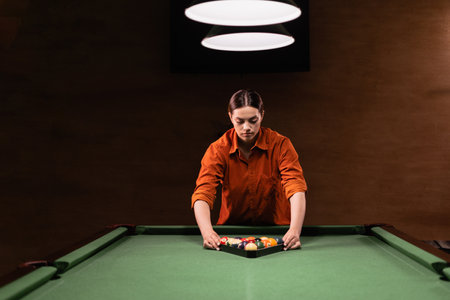 Sports game of billiards on a green cloth. Caucasian woman collect multi colored billiard balls in the form of a triangle with numbers shoot. Sports games, outdoor activities.の写真素材