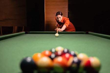 Cute woman with a cue aim at a billiard pyramid of balls, billiards game on. Billiard sports conceptの写真素材