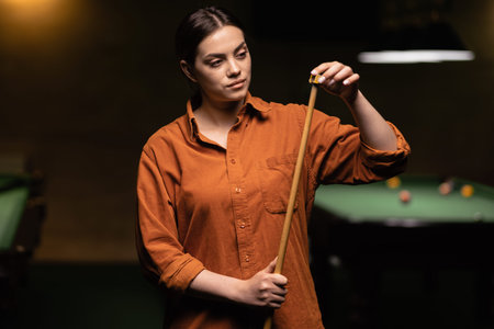 Beautiful woman billiard player, Snooker, chalking the cue in motion standing near green tables.