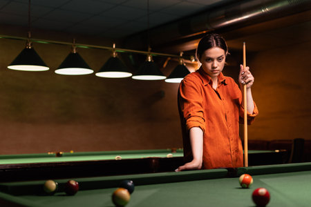 Beautiful girl playing billiards, learning to play billiards. Dark background. Pleasant pastime, alone rest, entertainment.の写真素材