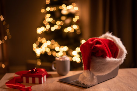 Christmas laptop in Santa hat standing on a table. Remote work on Christmas Eve. Online store, buying gifts for the winter holidays.の写真素材