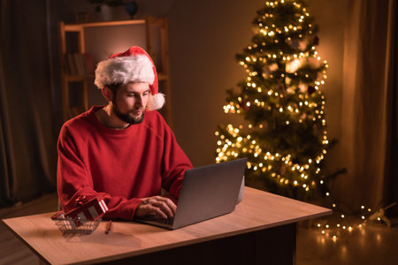 Smiling man sending e-mails or have shopping online on laptop on Christmas Eve at home.の写真素材