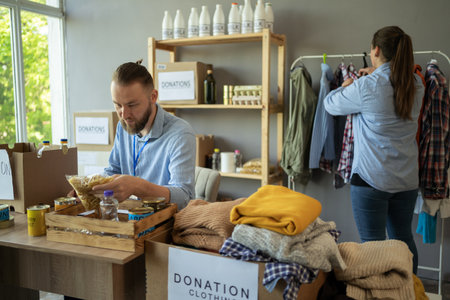 Volunteers collecting food and clothes donations in warehouse. Team of volunteers with donations boxes in a small warehouse. Volunteers putting clothes in donation boxesの写真素材