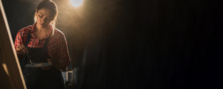 Beautiful female painter in dark art studio. Young talented artist working.の写真素材