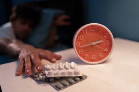 Insomnia concept. Sleepy man on bed take sleeping pill or night medicine. Suffering from insomnia. Glass of water on nightstand in bedroom.の写真素材