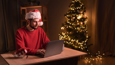 Young bearded man with gift and laptop. Online shopping at Christmas holidays. Freelance guy working from home office. Male typing at notebook computer. Christmas moments.の写真素材