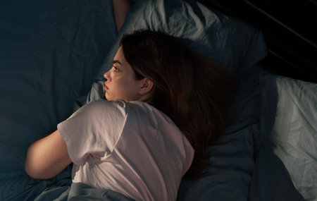 Young sad woman lying in bed late at night trying to sleep suffering insomnia sleeping disorder looking worried. Mental health conceptの写真素材