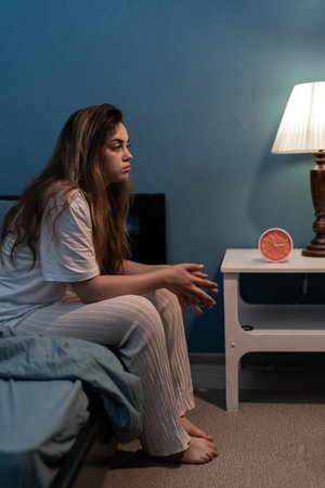 Woman sitting on bed suffering from insomnia and sleep disorder thinking about her problems at nightの写真素材
