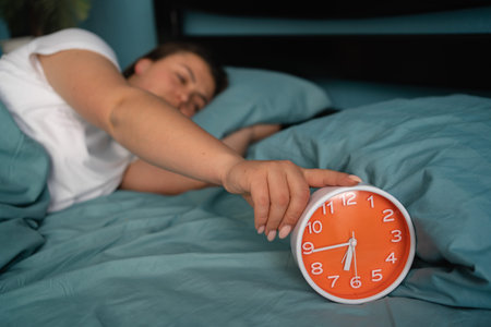 Girl lying in bed turning off an alarm clock on the morning