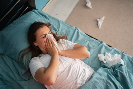 Woman sneezing and holding tissue, runny nose, flu symptoms. Healthcare and medical conceptの写真素材