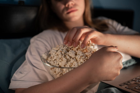 Young woman working or watching movie while eating popcorn looking at laptop screen