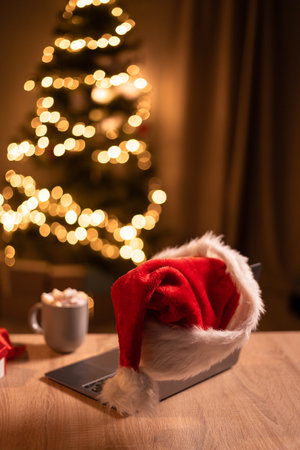 Laptop on table with Santa Claus hat in home office with christmas treeの写真素材